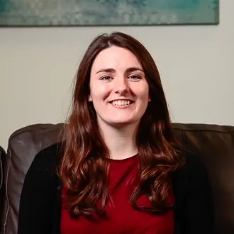 Headshot of Christina Thornton, ILS Finance Manager, sitting on a couch with a colourful painting in the background.