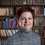 Elize Rossouw, an ILS case manager from East Grinstead, West Sussex stands in front of a bookcase wearing a cozy sweater.