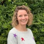 Based in Southampton, Hampshire ILS Case Manager Kate Trodd, stands in front of bushes wearing a star-patterned sweater.