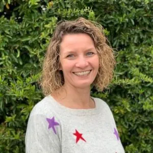 Based in Southampton, Hampshire ILS Case Manager Kate Trodd, stands in front of bushes wearing a star-patterned sweater.